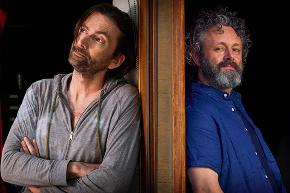 David Tennant in a grey hoody leans against a door, Michael Sheen wearing a blue shirt leans against the other side of the door