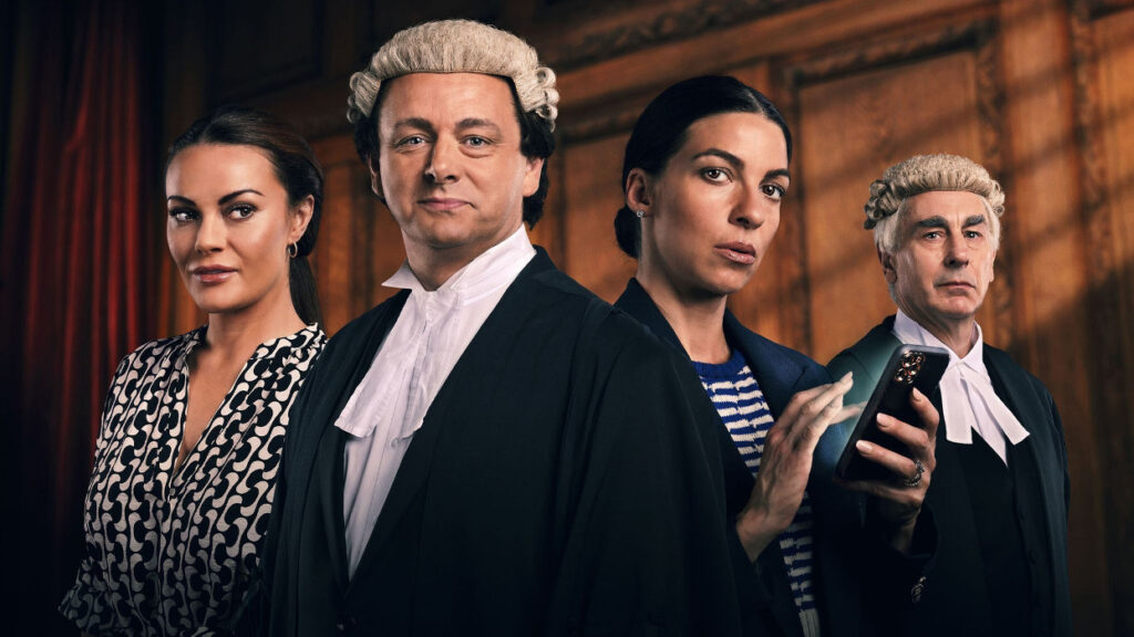 The actors from the drama stand in a courtroom dressed in their character's costumes, Michael Sheen is in a barrister's gown and wig.